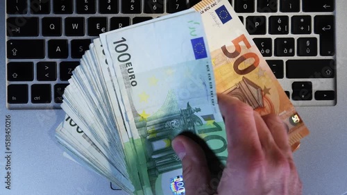 A man withdraws 10,000 euros in 100, 500, 50 eurbills from a laptop keyboard. Concept of earning with internet with online business or network marketing. Trading online. earn money with the internet