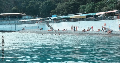 Tourists swim, sunbathe, and relax on a vibrant city beach. Perfect for summer holidays, vacations, and peak tourist season. 4K.