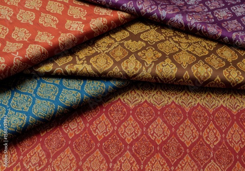 A flat lay of luxurious silk textiles adorned with the traditional Kanok flame pattern in various vibrant colors, showcasing textile artistry