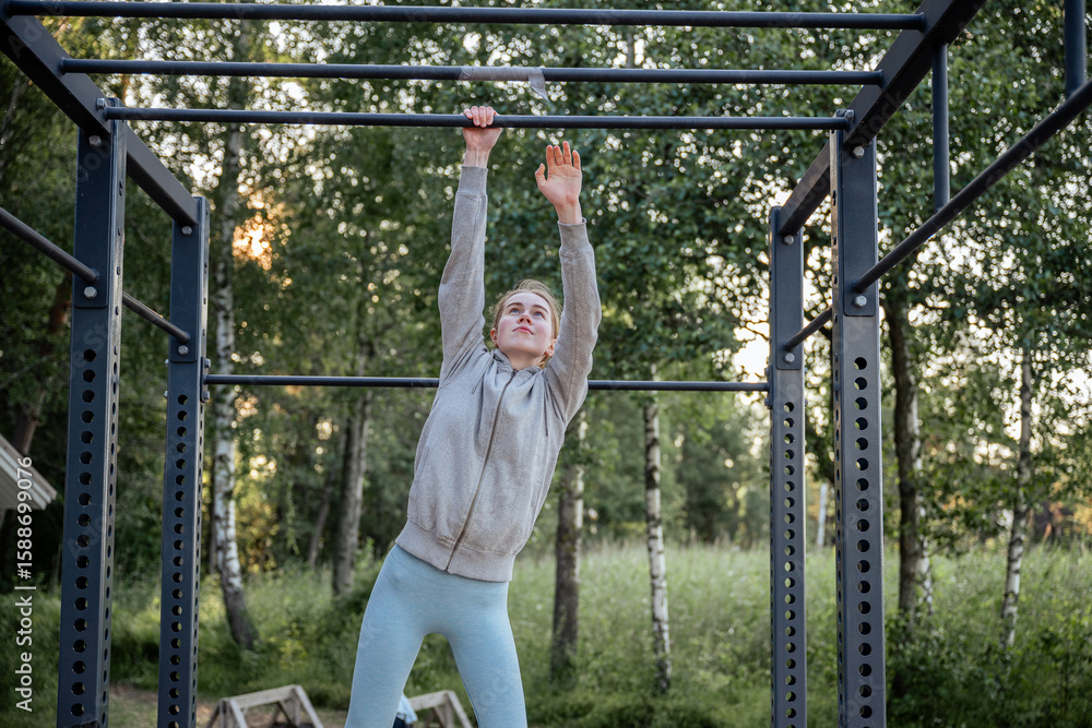 Fototapeta premium Young woman hanging on pull-up bar at outdoor gym in park