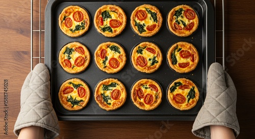 Freshly baked mini quiches on a tray, held by oven mitts, ready to serve.