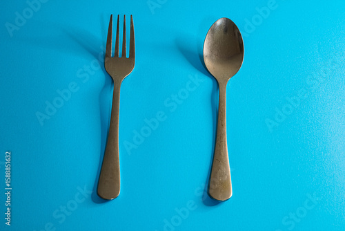 A fork and spoon are positioned side-by-side on a bright blue surface, casting shadows.