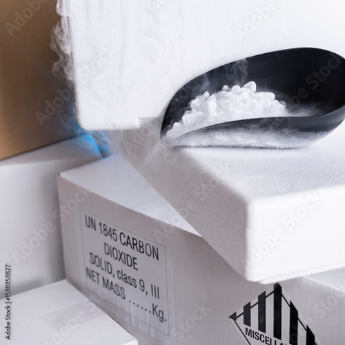 Black scoop with dry ice pellets creating visible vapor fog from shipping container with labels