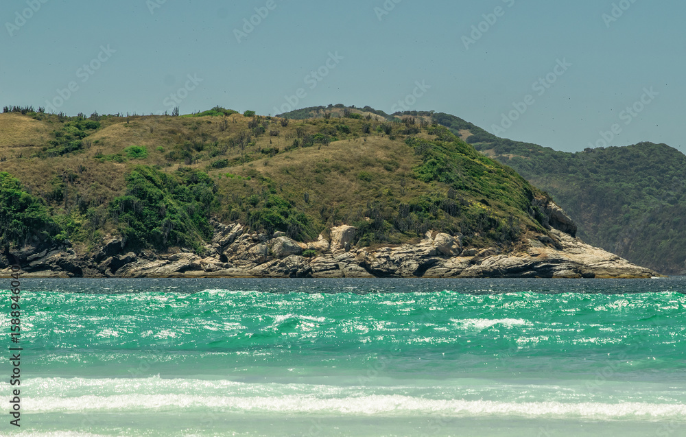 Fototapeta premium Beautiful beach das Conchas, close to the city of Cabo Frio, with blue sea around, sky with clouds and mountains in the background.