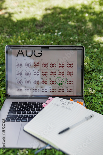 Bilde på lerret Close-up of laptop in green grass displaying August calendar marked with hard work days and one day off