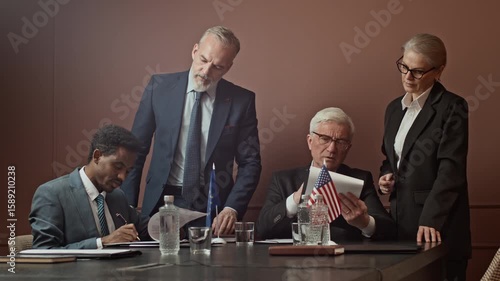 Wide shot of group of diverse representatives and attache examining and signing business contracts sitting at table during intergovernmental meeting