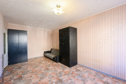 room interior featuring two dark wardrobes, a small sofa, and patterned flooring. The walls are light pink with vertical stripes. A ceiling light illuminates the space