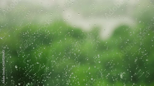 Close-up of rain droplets on a glass window, showcasing blurred green foliage outside, creating a tranquil and refreshing ambiance