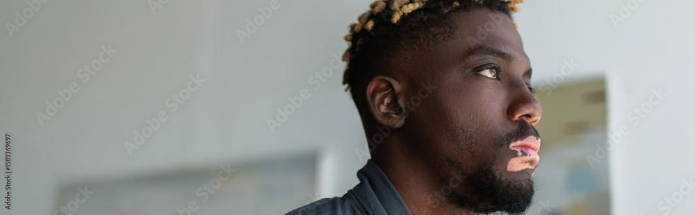 Fototapeta premium Young african american man with vitiligo looking away at home, banner