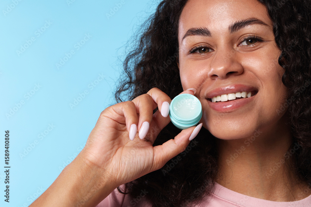 Smiling woman with lip balm on light blue background Smiling woman with lip balm on light blue background