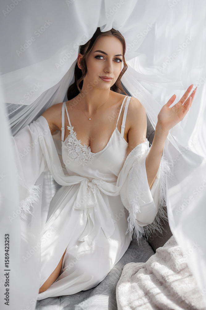 Bride in elegant white gown poses gracefully under flowing fabric indoors Bride in elegant white gown poses gracefully under flowing fabric indoors