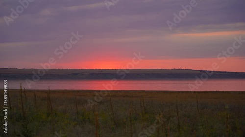 Serene summer landscape with soft pink and purple sunset sky above a quiet river, peaceful atmosphere and distant horizon in the evening light 