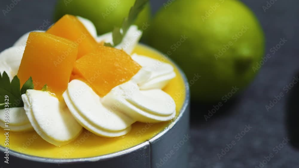 Creamy mango mousse cake topped with whipped cream, fresh mango slices, and parsley, resting on a dark surface with a lime in the background, offers a vibrant dessert presentation Creamy mango mousse cake topped with whipped cream, fresh mango slices, and parsley, resting on a dark surface with a lime in the background, offers a vibrant dessert presentation