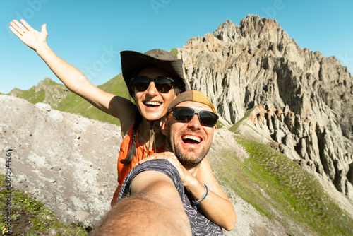 Cheerful couple of hikers friends taking selfie on top of mountain. Millennial guy girl enjoying summertime day out trip laughing at camera together - Millennial travelers standing in scenic nature