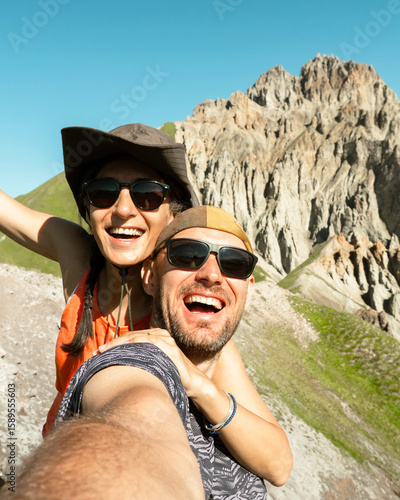 Cheerful couple of hikers friends taking selfie on top of mountain. Millennial guy girl enjoying summertime day out trip laughing at camera together - Millennial travelers standing in scenic nature