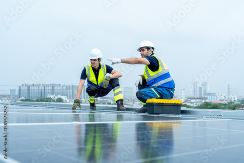 Two engineer or technician worker discuss together during work with solar cell panel on rooftop of factory building and look like rain coming.