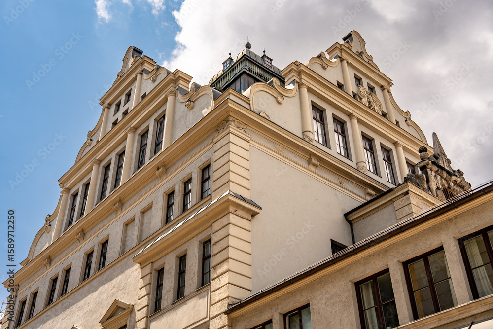 Obraz premium Historic Bavarian Architecture In Munich: Yellow Corner Building With Green Dome Tower, Ornate Windows, Flower Boxes, And Steep Roof Under Dramatic Cloudy Sky In European Urban Landscape
