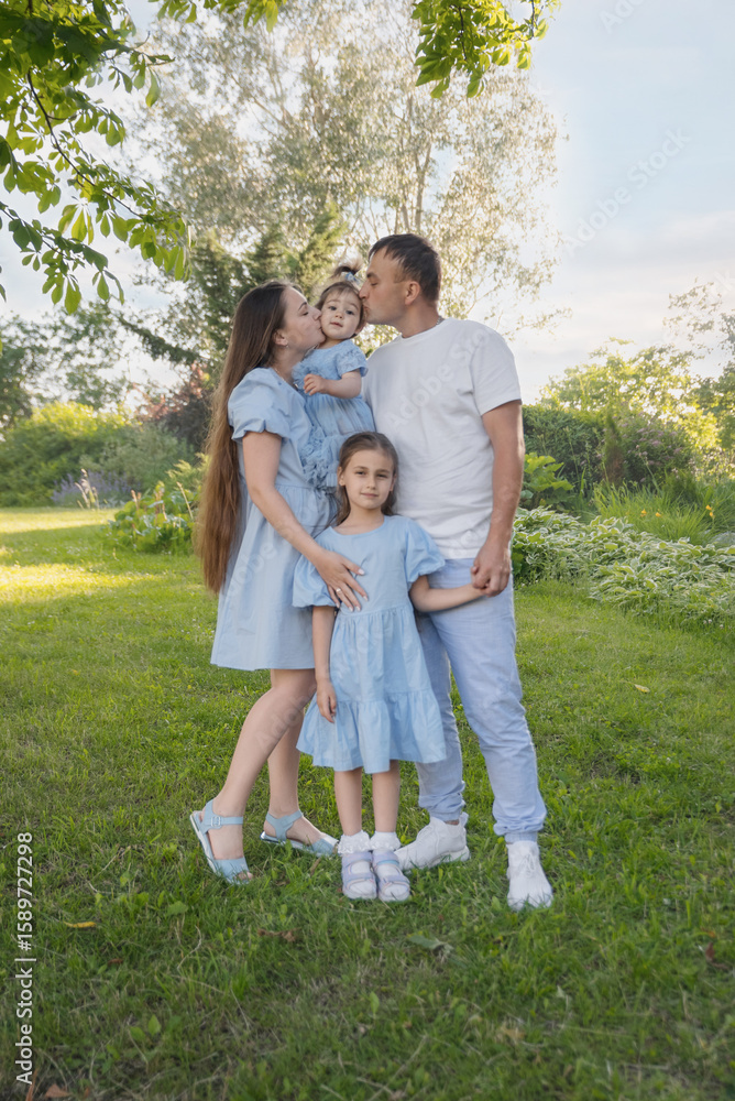 A happy family in nature. The family has two daughters. The family is dressed in blue clothes, and everyone is looking at the camera. A happy family in nature. The family has two daughters. The family is dressed in blue clothes, and everyone is looking at the camera.