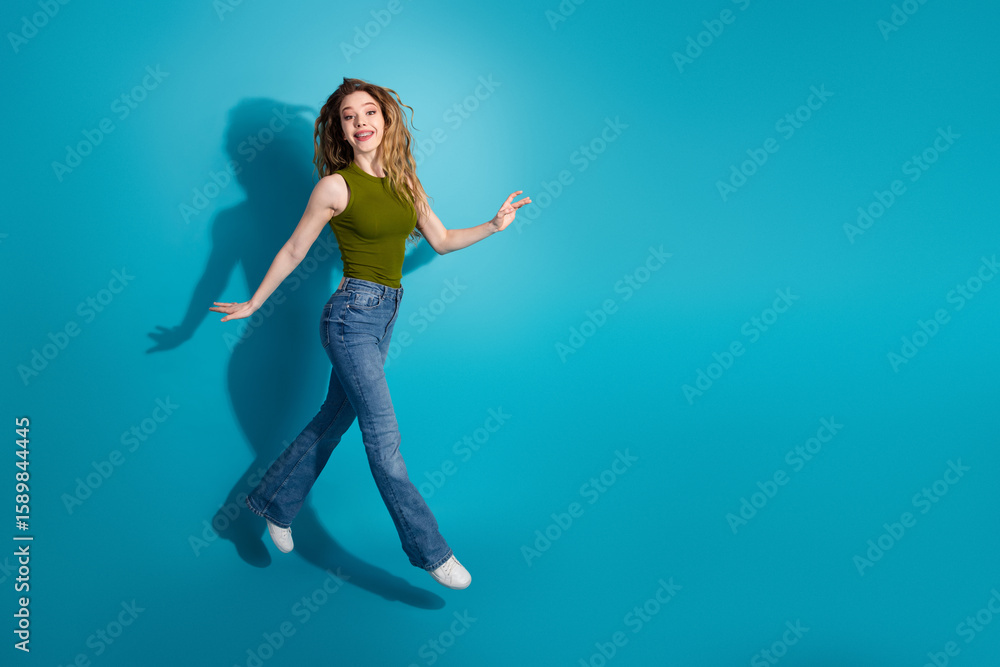 Obraz premium Excited young woman in casual outfit, showcasing dynamic energy and trendy style against a bright blue background.