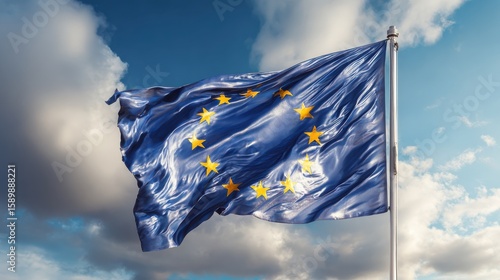 European Union Flag waving in the wind on flagpole over a blue and cloudy sky.
