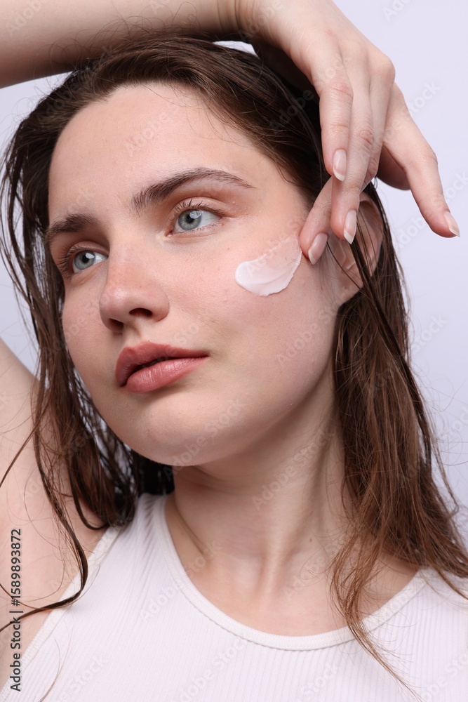 Fototapeta premium Beautiful woman applying skincare product onto her face on light grey background, closeup