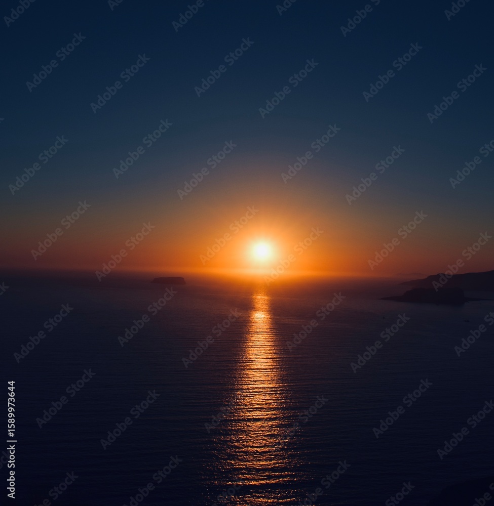 Naklejka premium Stunning ocean sunset with vibrant orange and blue sky reflecting on calm water.