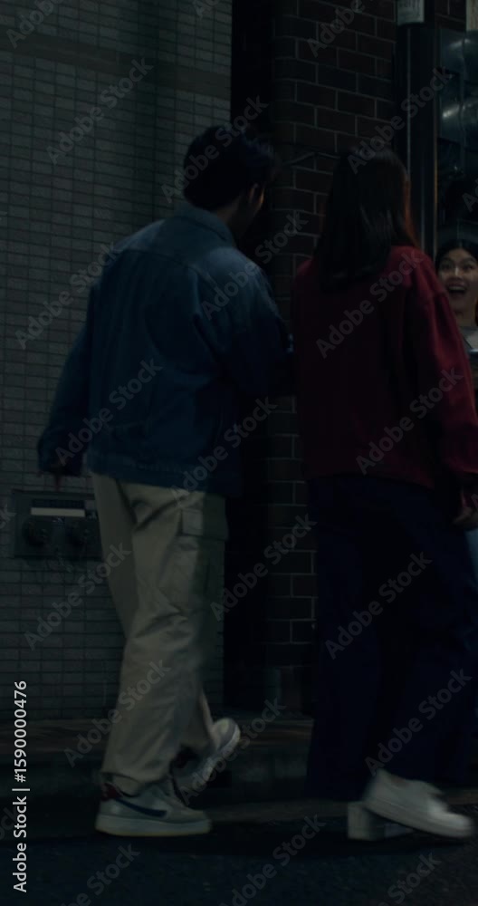 A young man and a woman meet their friend walking along a night street. They hug each other happily, greeting each other. A young man and a woman meet their friend walking along a night street. They hug each other happily, greeting each other.