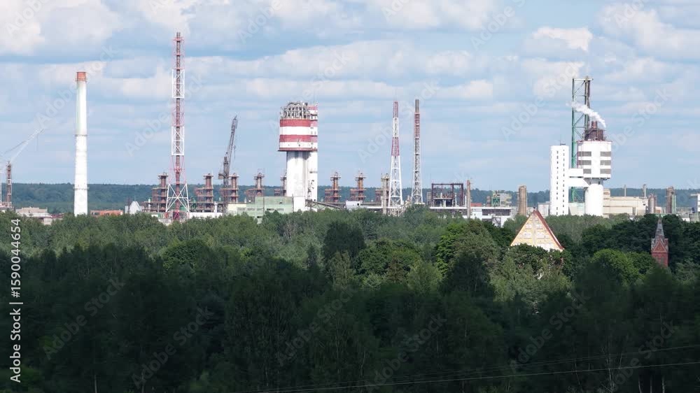 Wide shot of a large industrial complex surrounded by dense forest. Multiple smokestacks and towers dominate the scene. Some chimneys emit smoke, indicating active operation. Clear sky overhead. Wide shot of a large industrial complex surrounded by dense forest. Multiple smokestacks and towers dominate the scene. Some chimneys emit smoke, indicating active operation. Clear sky overhead.
