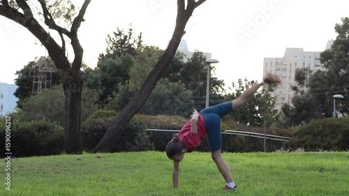 European blonde schoolgirl doing acrobatics, cartwheel on one hand, during physical education class outdoors, children at primary school in summer