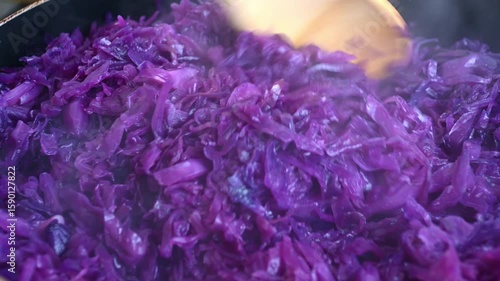 Stirring vibrant purple cabbage cooking with wooden utensils in closeup sequence