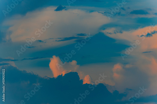 Fotografia Dramatic cumulus clouds lit by golden sunset light against a darkening blue sky, creating a moody and atmospheric scene
