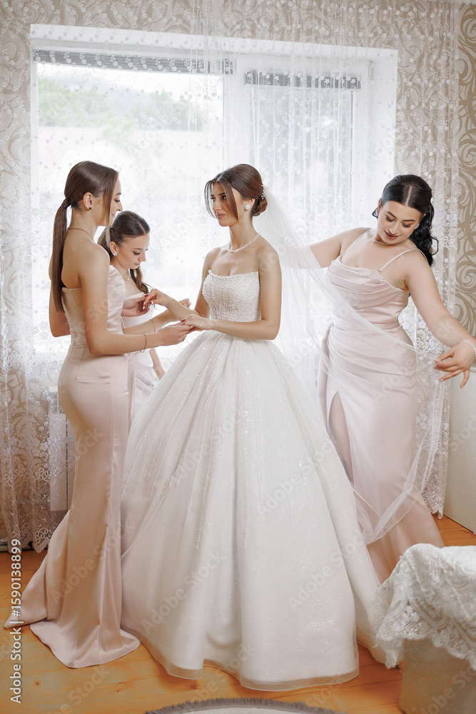 Fototapeta premium Bride prepares for wedding with friends in elegant dresses in bright room