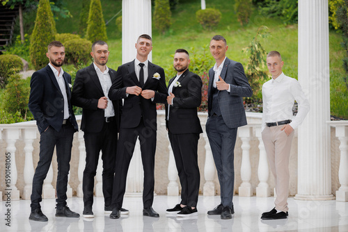 Φωτογραφία Groom and groomsmen pose together in formal attire at outdoor venue before weddi