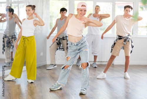 Canvas Print Girl in baseball cap with two hair pigtails with group of teenage friends, learn to dance hip hop in choreographic hall