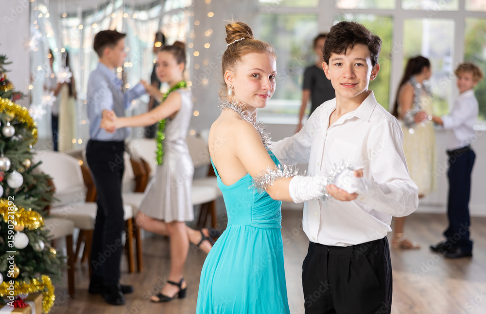Obraz premium Positive teen boy and girl are dancing classic version of waltz in couple during lesson at studio in New Year atmosphere. Leisure activities and physical activity for positive children.