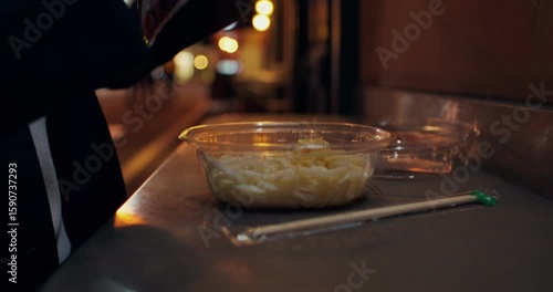 An elegant woman prepares to eat takeaway food while standing on the street of the night city. Close-up of her hands, unrecognizable person