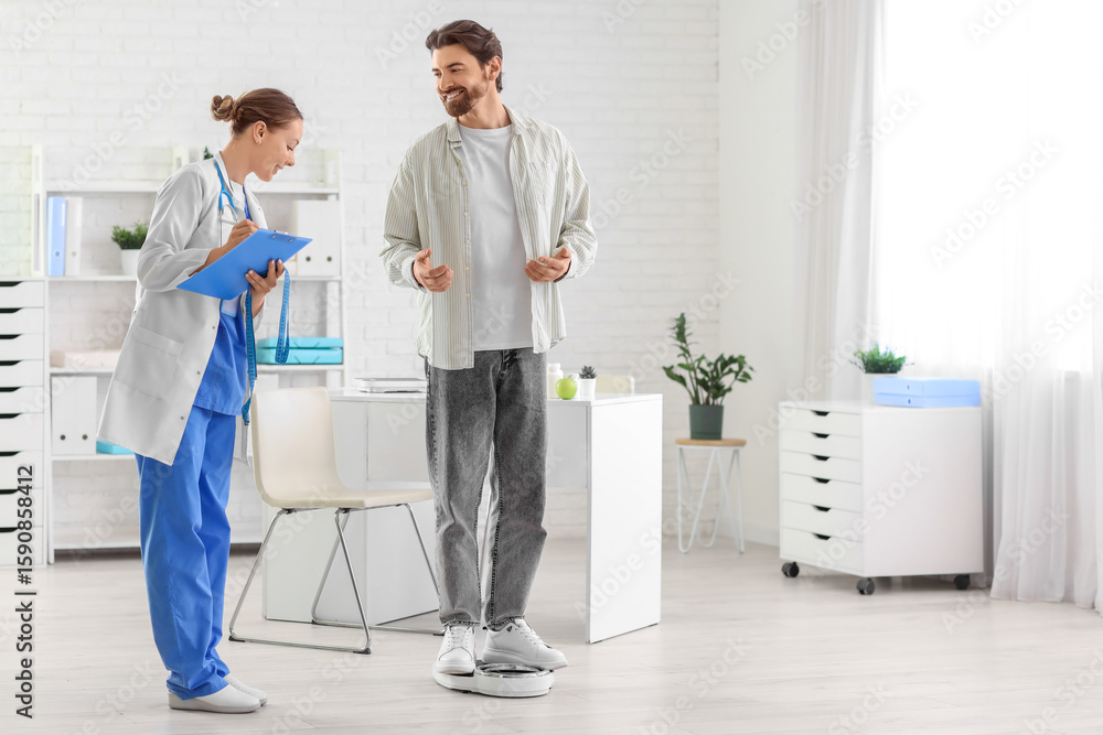 Fototapeta premium Young man measuring weight on scales with nutritionist in clinic