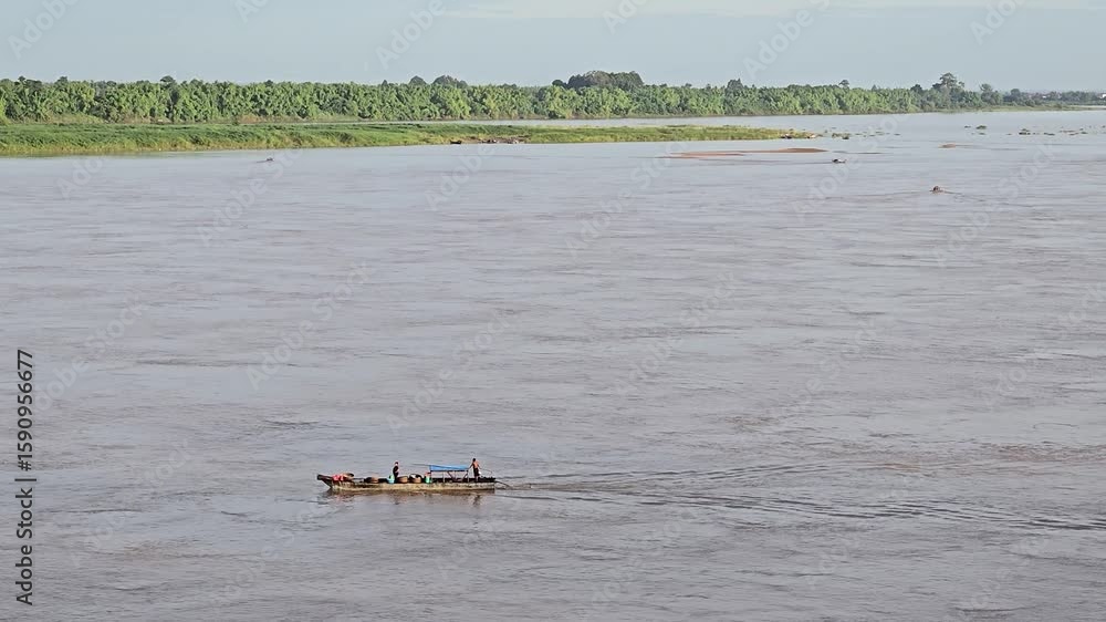 Kracheh, Cambodia - 29 June 2025. A small cargo boat carrying barrels and two people navigates the Mekong River in broad daylight. Kracheh, Cambodia - 29 June 2025. A small cargo boat carrying barrels and two people navigates the Mekong River in broad daylight.