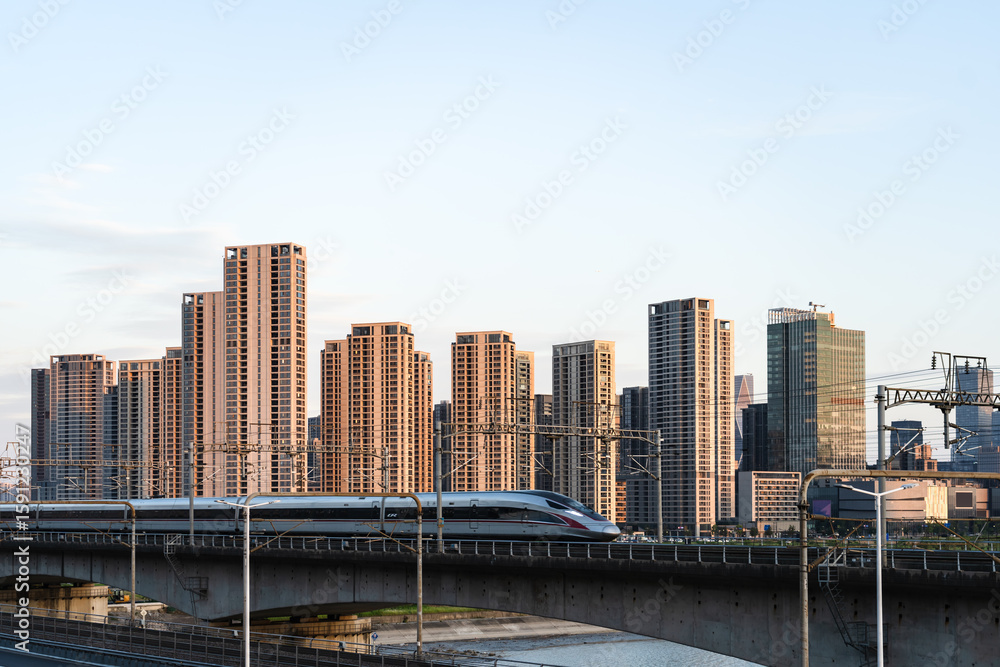 Obraz premium Under the setting sun, high-speed trains run through the modern urban area, embodying the concepts of urban speed and transportation