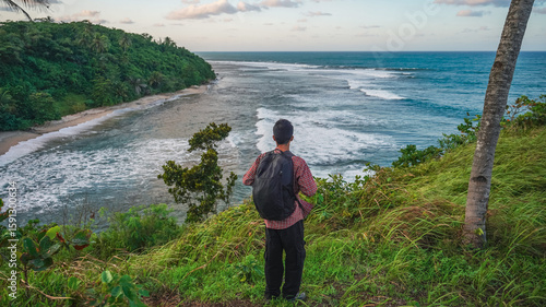 Photos Solo hiker on grassy bluff above ocean waves, tropical sky and palm trees swaying gently