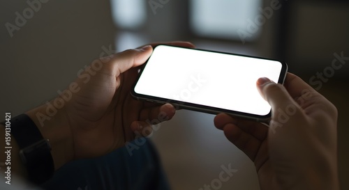 Close up of a person holding a mobile phone with a blank white screen in landscape orientation indoors.