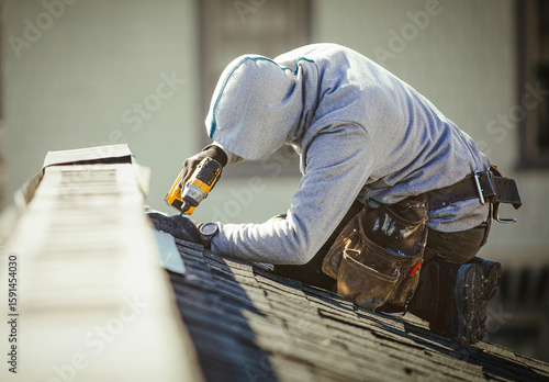 Roofer with a drill fixes a roof in a residential area