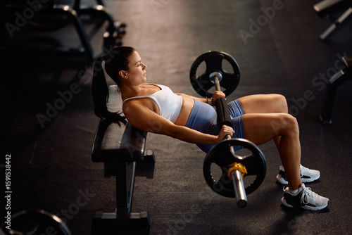 Schilderij op canvas Athletic woman doing barbell hip thrust exercise while working out in gym