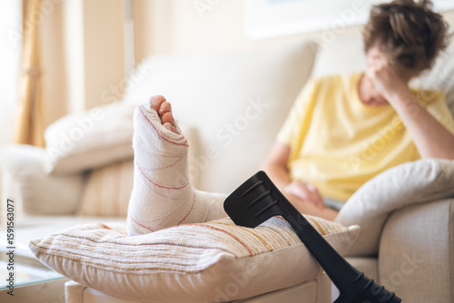 Fotografie Patient is recovering at home with a broken leg in a cast, resting on a pillow w