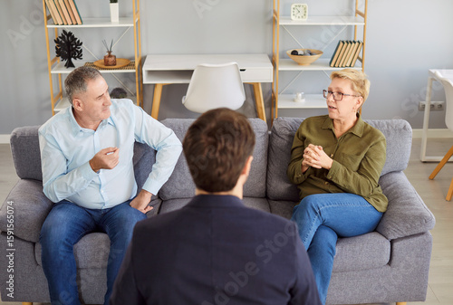Canvas Print Serious elderly family couple attending a therapy session, engaging in conversation with a psychologist to resolve conflicts or quarrel