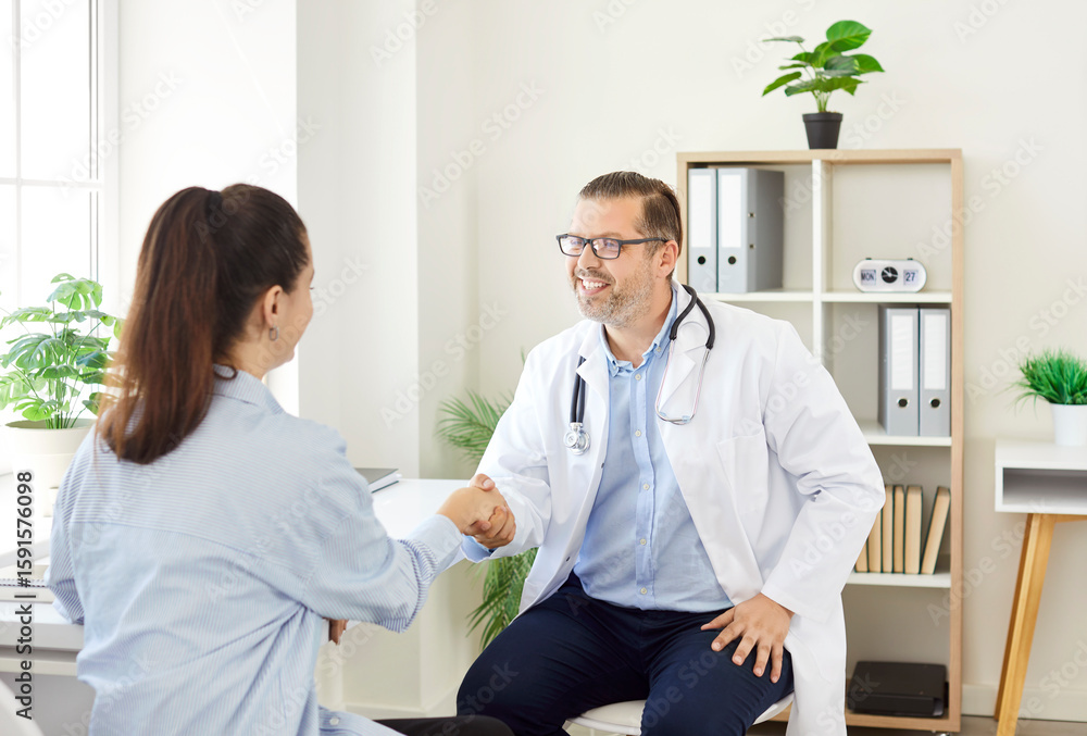 Obraz premium Smiling and happy doctor or nurse shakes hands with a female patient during visit to the hospital. Medical healthcare, trust, and professional care provided in the clinical environment.