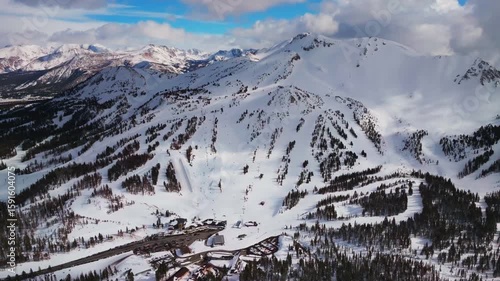 Groomed ski trail runs Main Lodge parking lot Mammoth Mountaini resort California aerial drone gondola chairlift skiing snowboarding terrain park half pipe winter sunny blue sky forward pan up motion