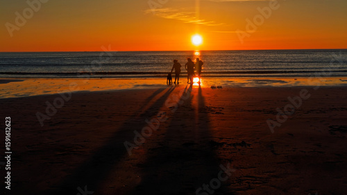 Three people and a dog in silhouette at the vibrant Midnight Sun beach. Lofoten Islands, Northern Norway