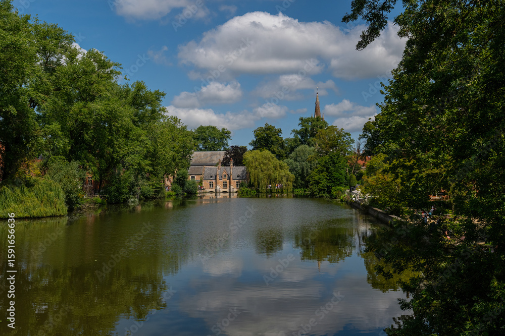 Fototapeta premium This scenic view of Bruges reflects the historic buildings and lush vegetation reflected in the calm waters, evoking the charm of the Middle Ages and peaceful beauty.