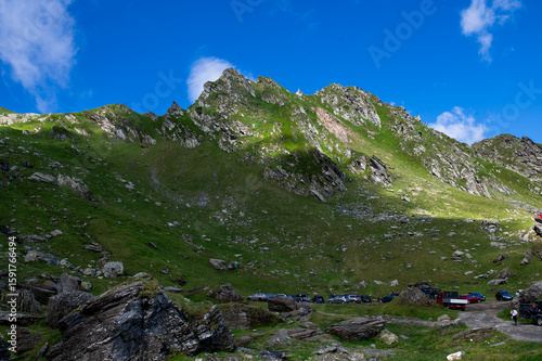 Green mountain slope with rocky formations under a bright blue sky in the Făgăraș Mountains, Transfăgărășan, Romania.